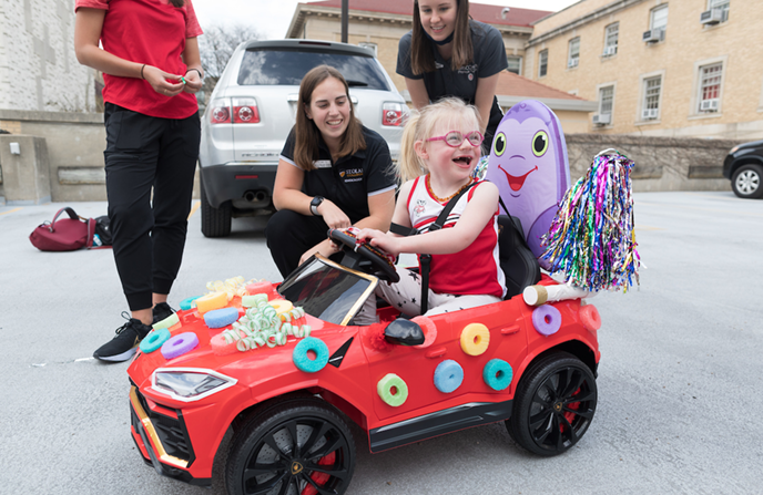 DPT students smiling with a child sitting in a modified youth-sized car