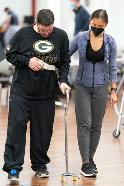 A patient, walkiung with a cane, receives guidance from a DPT student