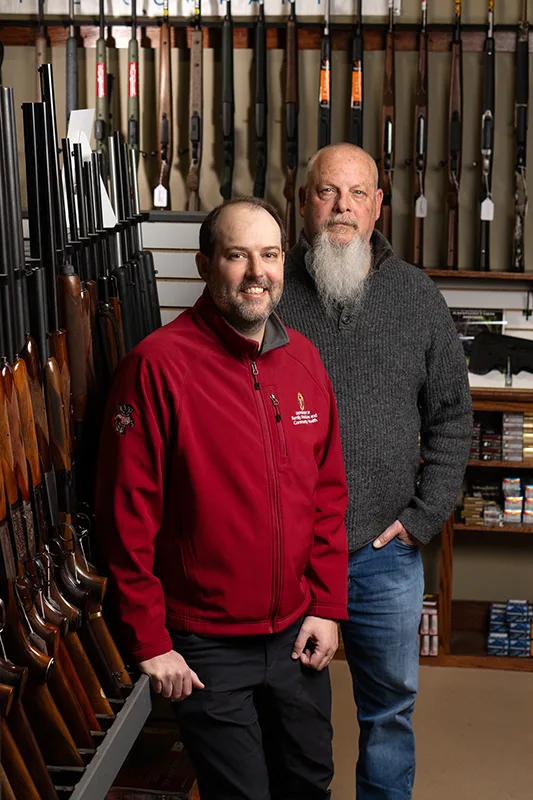 Two men posing for a picture inside a gun store