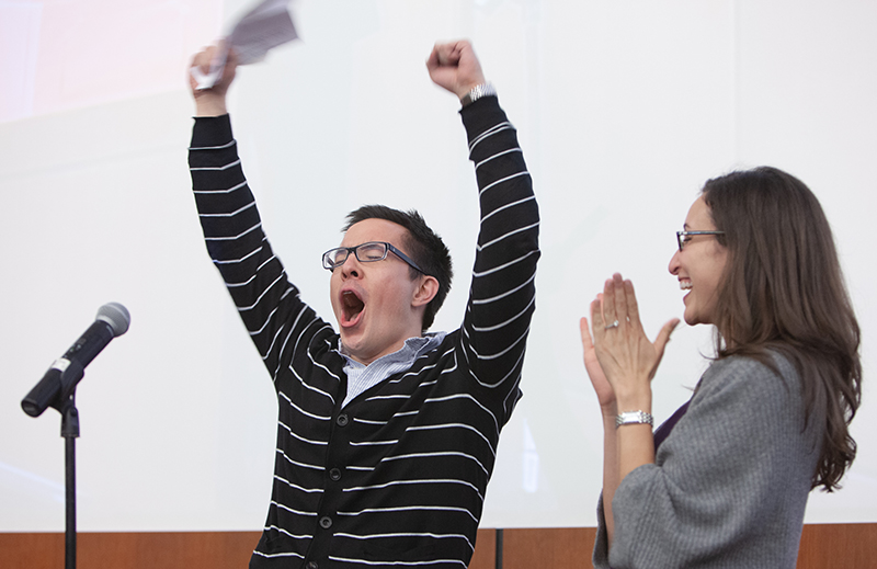 A man cheers with his hands in the air while a woman looks on while clapping
