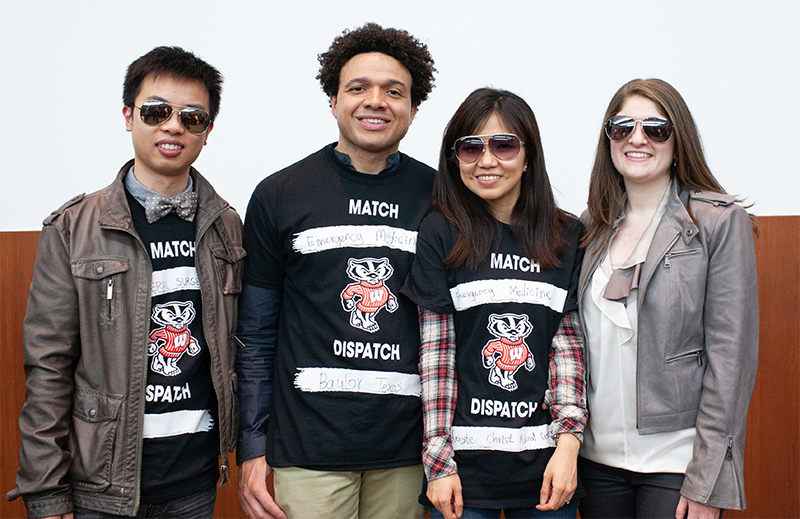 A group of four people stand together wearing a combination of black t shirts and sunglasses at a Match Day event