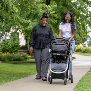 Two women smile while walking outside with a stroller