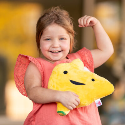 Transplant recipient Lucy Sughroue smiles while flexing her muscles and holding a stuffed toy