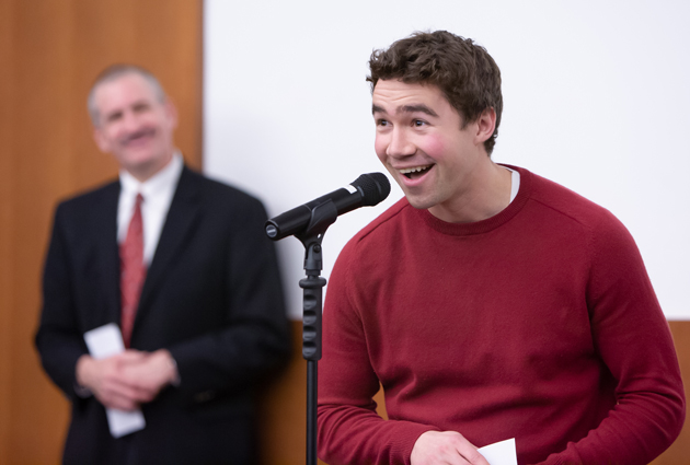 A man in a dark red sweater stands in front of a microphone