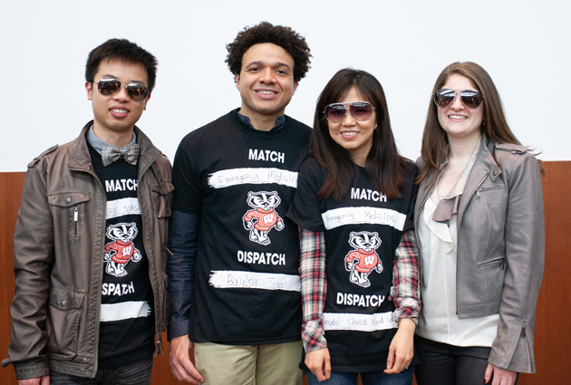 A group of four people stand together wearing a combination of black shirts and sunglasses at a Match Day event