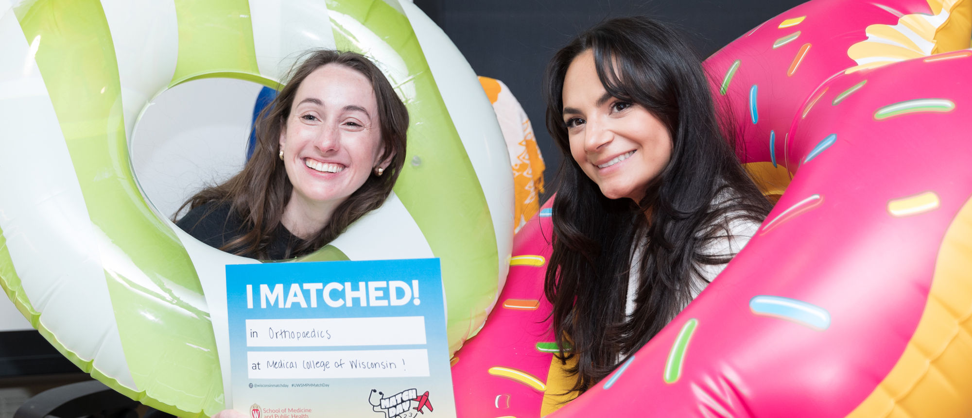 Two women pose with inflatable pool donuts during the Match Day 2023 event
