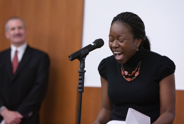 A woman stands in front of a microphone with an excited expression on her face