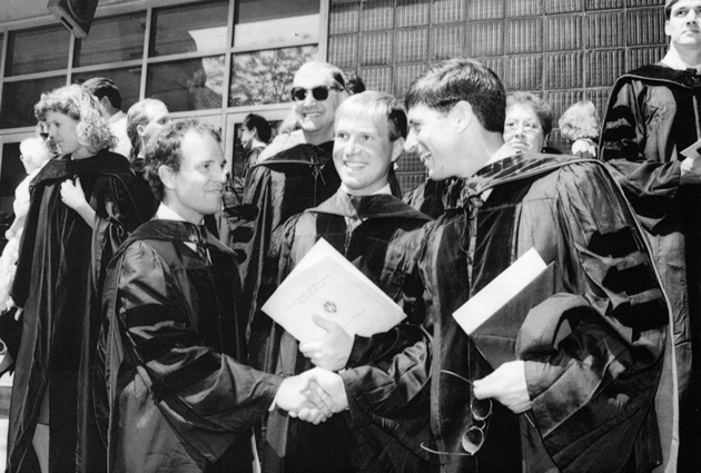 Three men shake hands at a graduation event