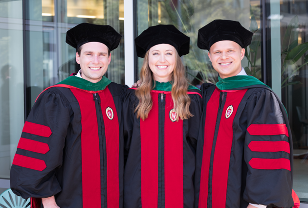Three people wearing graduation caps and gowns stand close together and smile