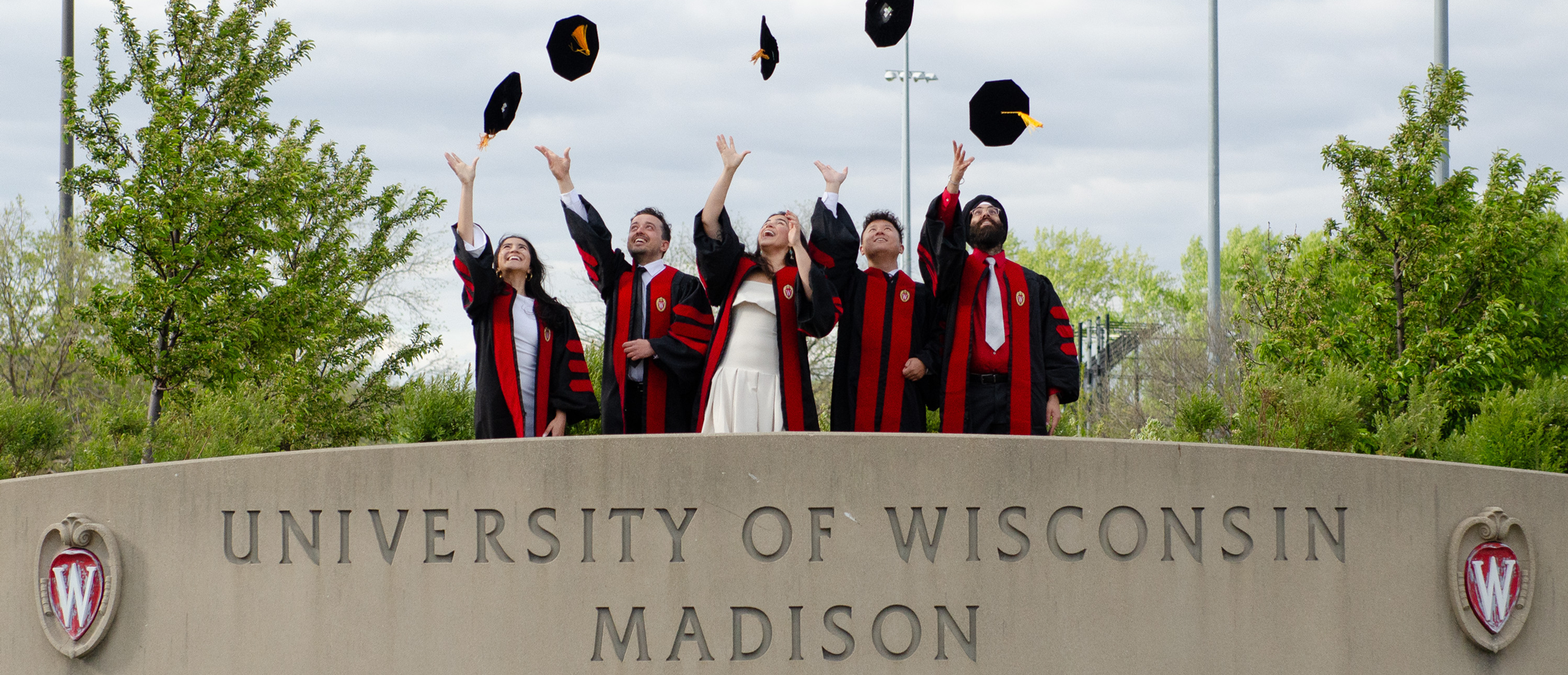 A group of five people throw their caps in the air at a graduation event