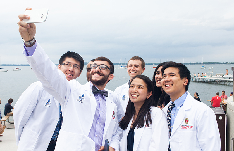A group of people wearing white medical coats take a group selfie