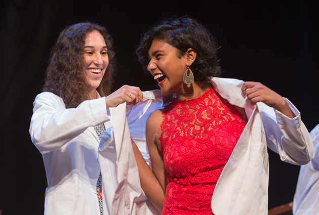 A woman receives a white medical coat during a ceremony