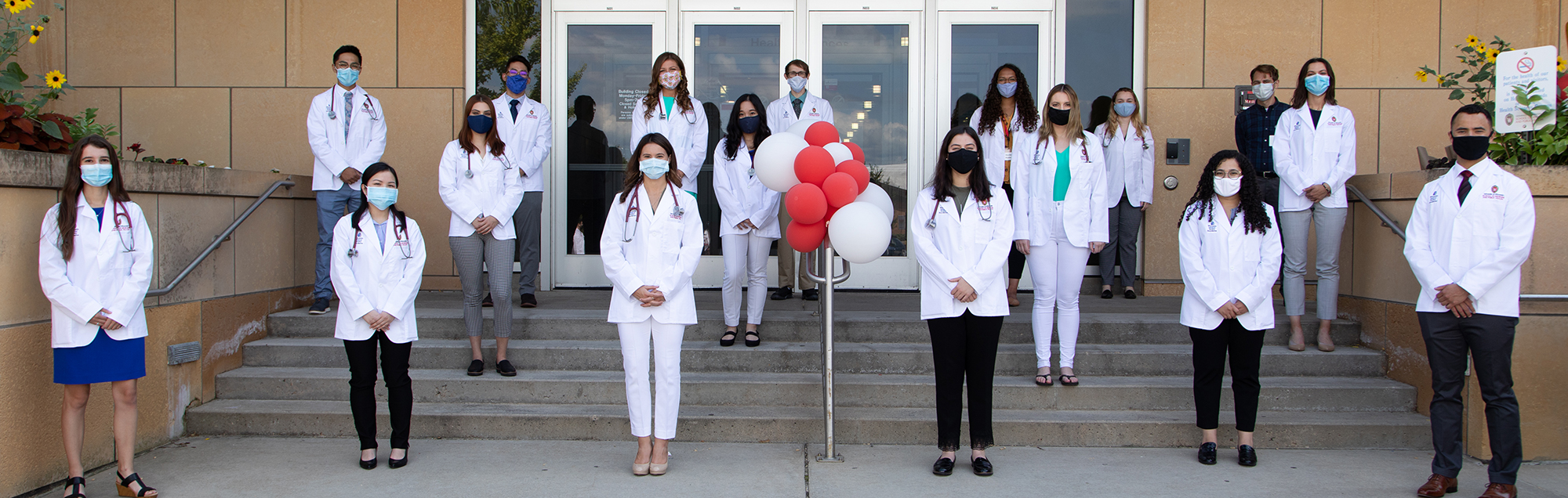A large group of people wearing face masks and medical coats stand outside togehter