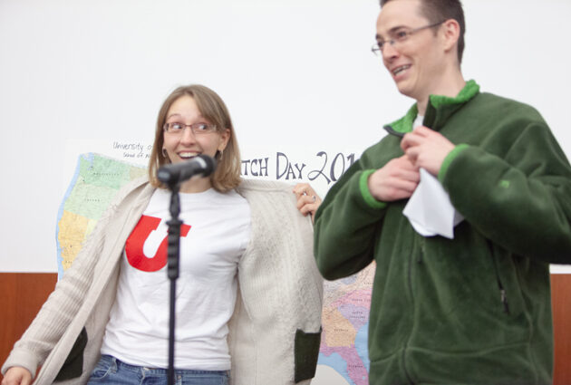 A man and a woman stand together, the woman has a red letter u on her white t shirt