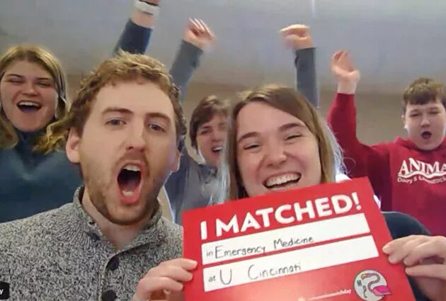 A woman holds up a sign for Match Day 2020 with a group of cheering onlookers