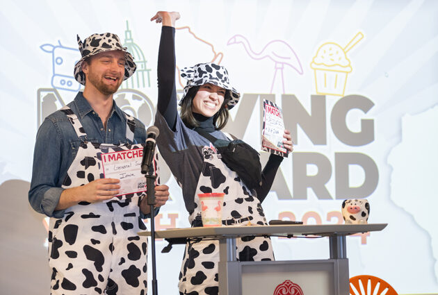 A man and a woman stand at a podium wearing cow print overalls and cow print bucket hats during the 2024 Match Day event