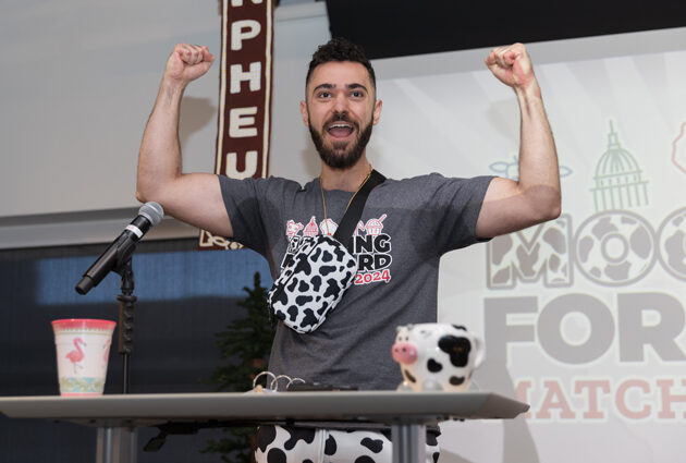 A man stands at a podium flexing his arms during the 2024 Match Day event