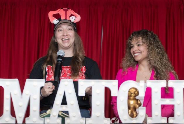 Two women stand behind a sign that says Match at the 2025 Match Day event