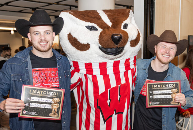 Two men wearing cowboy hats stand on either side of Bucky Badger at the 2025 Match Day event