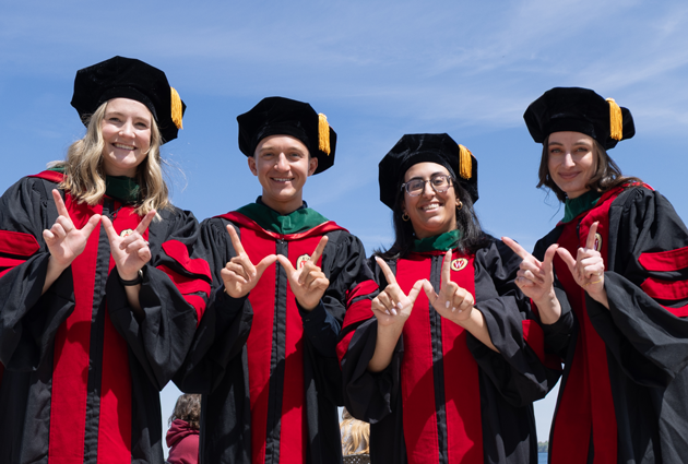 A group of four people in graduation caps and gowns pose for a photo and display a "w" on their hands