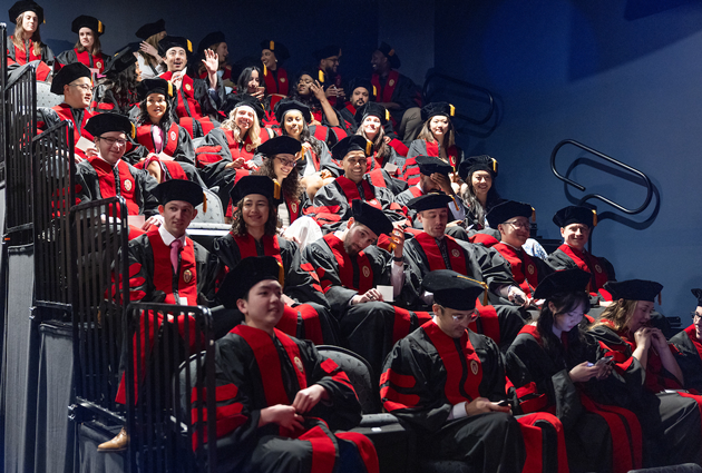 A large group of graduates sit together on bleachers