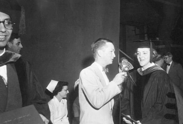 Two people stand on stage during a graduation event