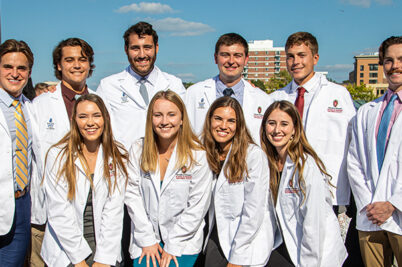 A group of ten people stand together wearing white medical coats