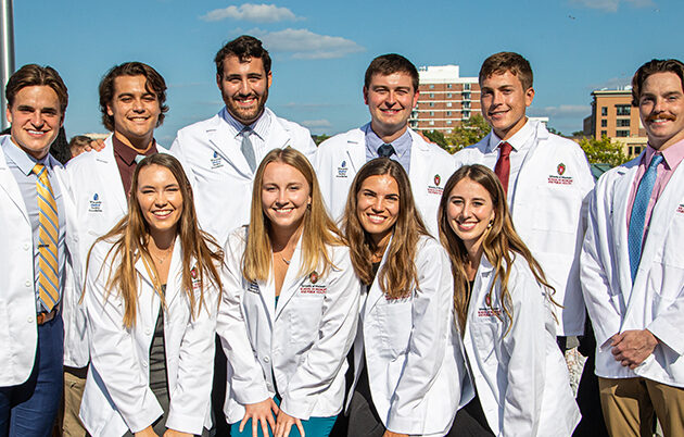 A group of ten people stand together wearing white medical coats