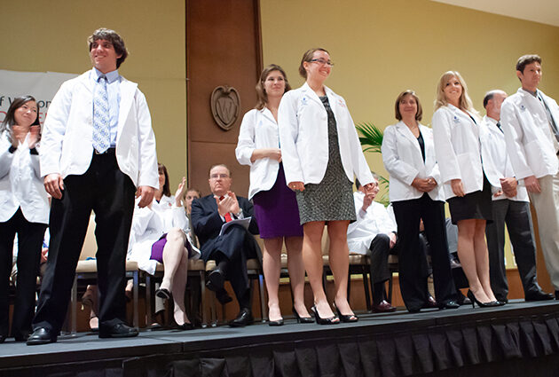A group of people stand together on a stage wearing white medical coats