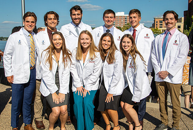 A group of ten people stand together wearing white medical coats