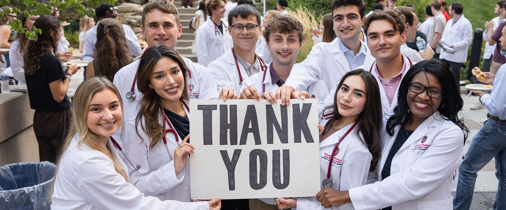 Medical students white coats hold a sign that says thank you.