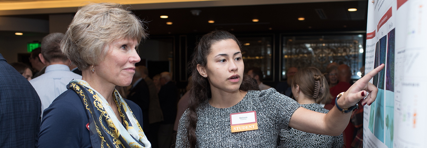 A poster session attendee listening to a student discuss their work