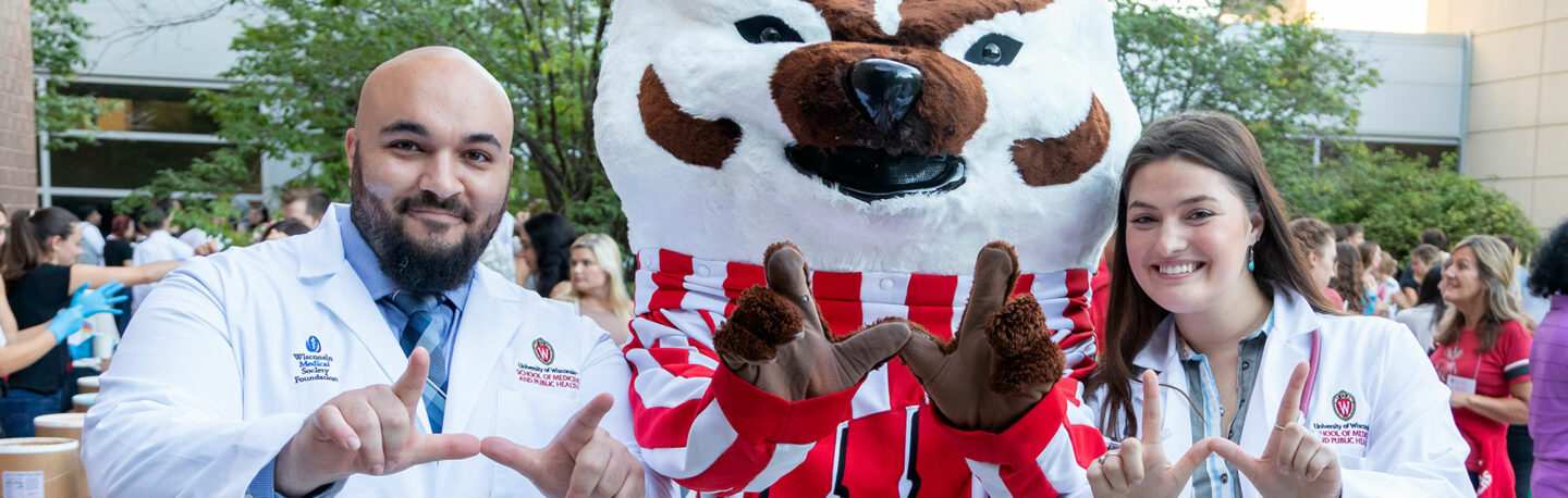 Medical students pose in their white coats with Bucky Badger