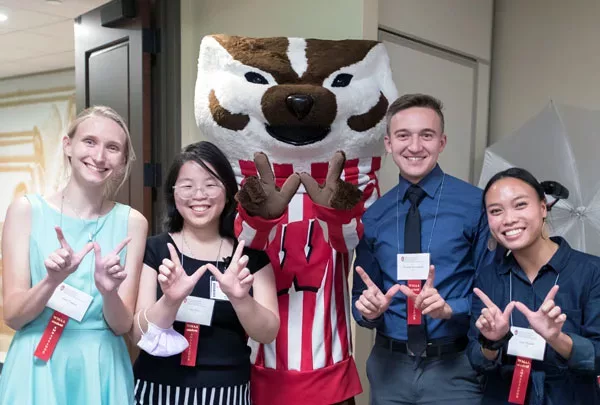Group of smiling 2022 Medical Student Ambassadors make Ws with their hands, alongside Bucky Badger