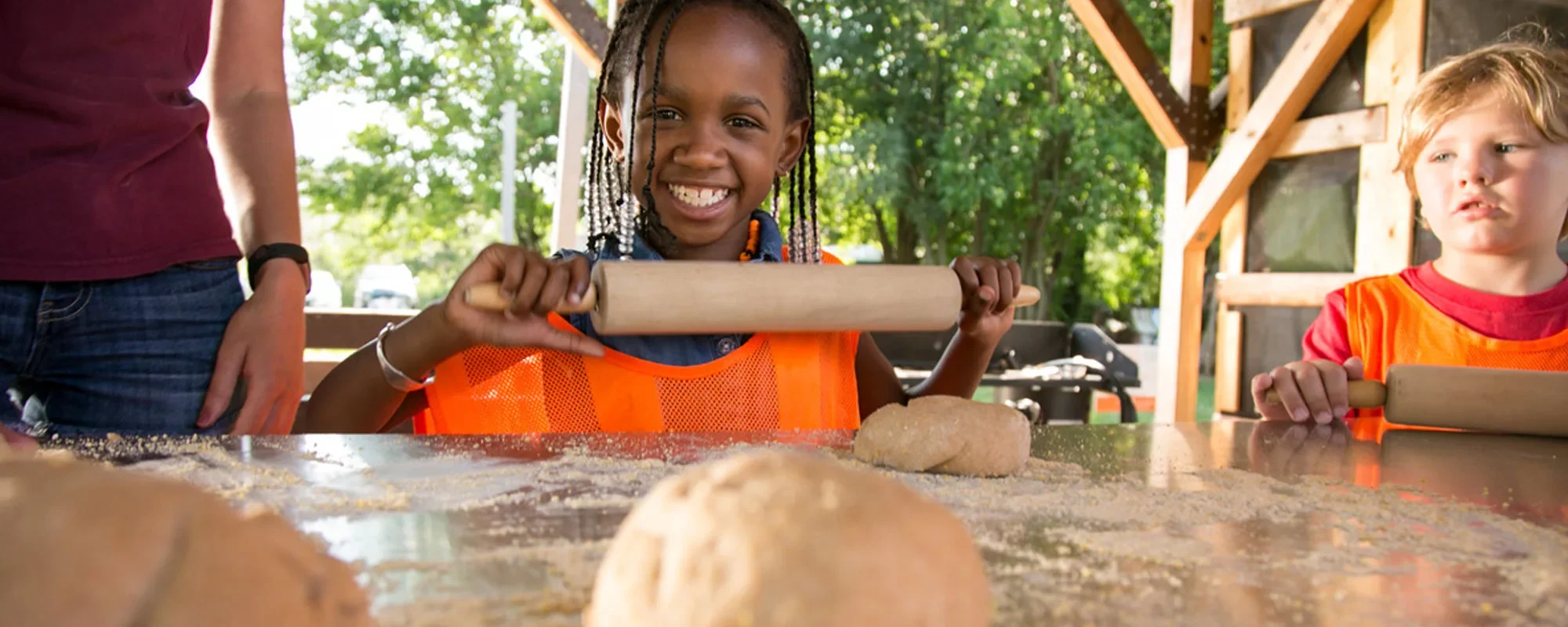 kids smiling and rolling out pizza dough at Troy Kids' Gardens