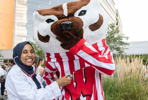 A first-year medical student smiling big while posing next to Bucky Badger