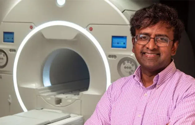 A researcher posing for a photo in front of an MRI machine