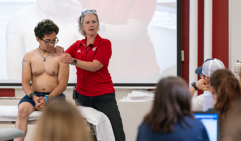 A DPT instructor demonstrates palpation skills on student's shoulder in front of a class