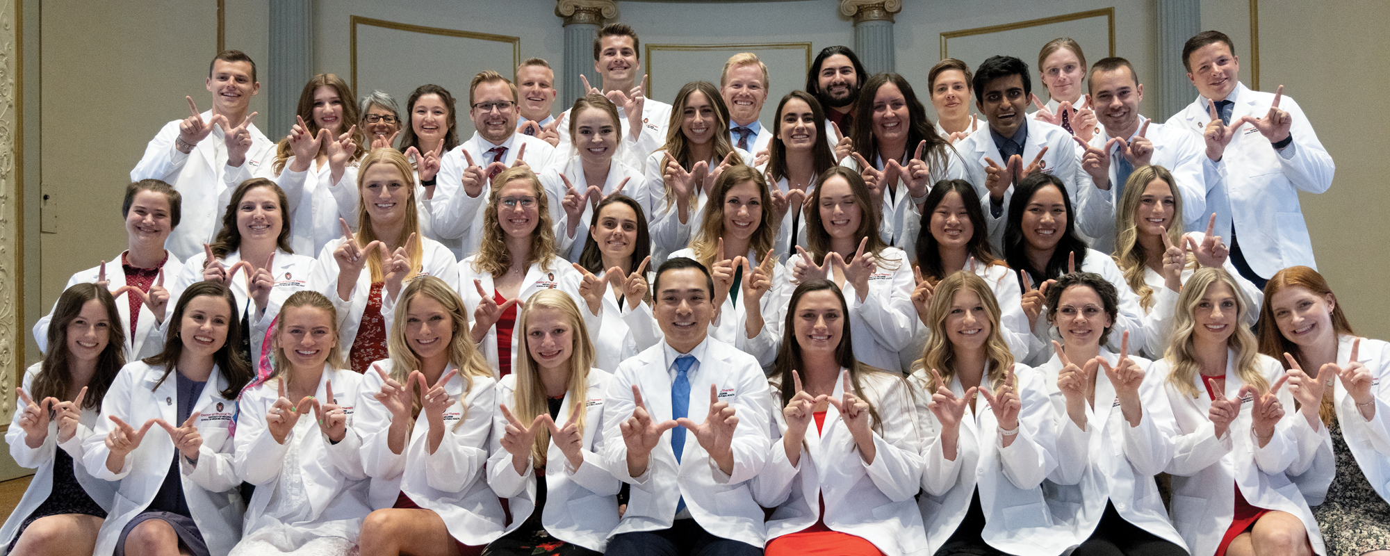 Group of smiling Doctor of Physical Therapy program students, in their white coats, make Ws with their hands