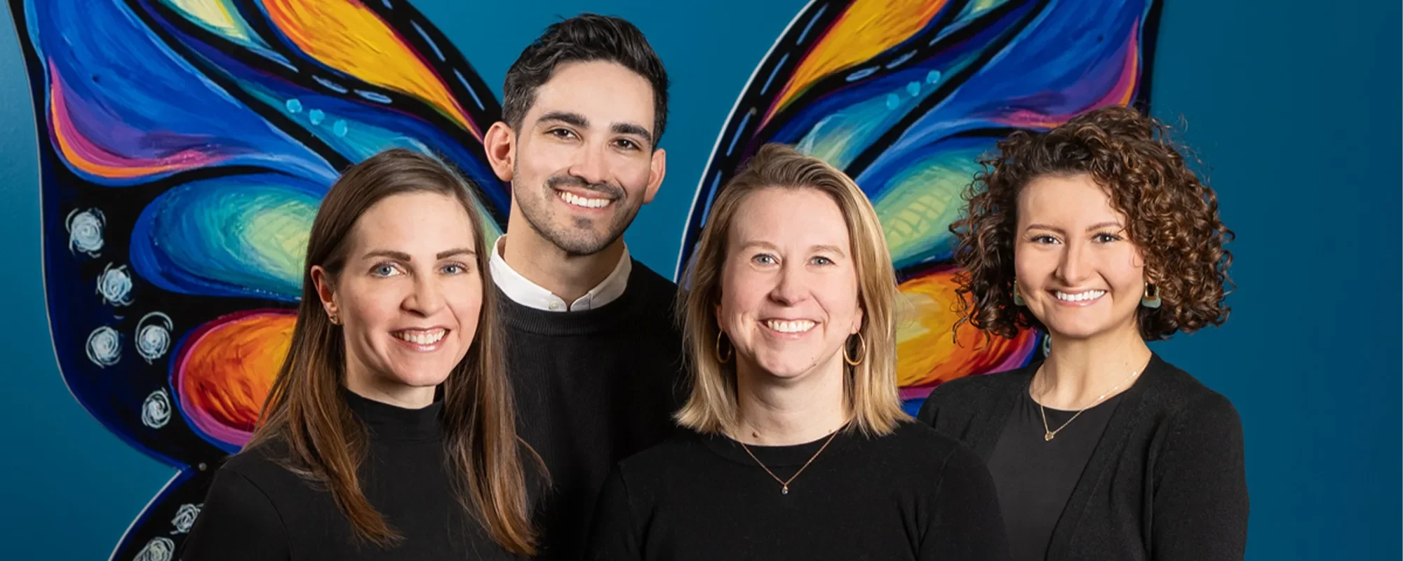 Four smiling TRIUMPH faculty and staff members pose in front of a butterfly mural