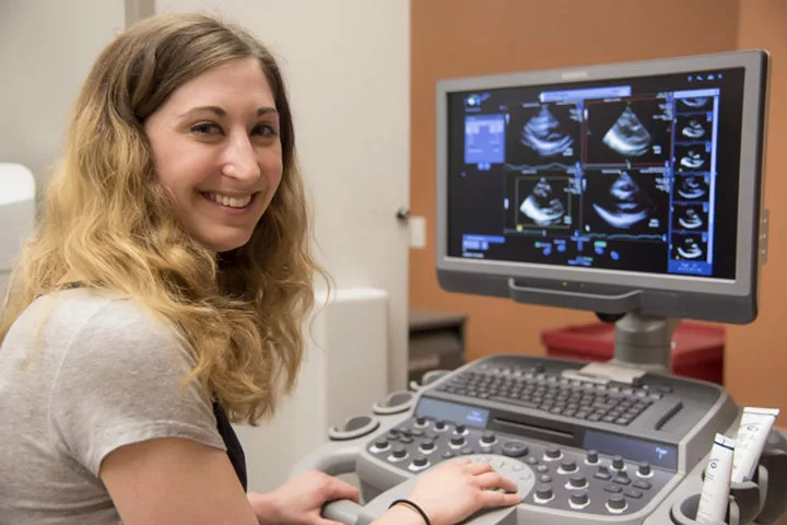 A researcher smiling for the camera while next to a screen displaying ultrasound images