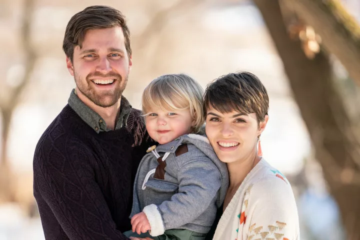 Two parents holding a young child between them, all smiling for the camera