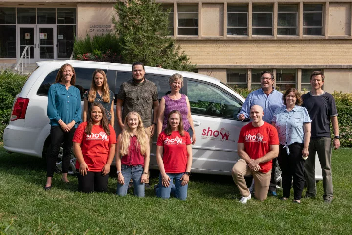 People posing in front of a van marked with the SHOW logo