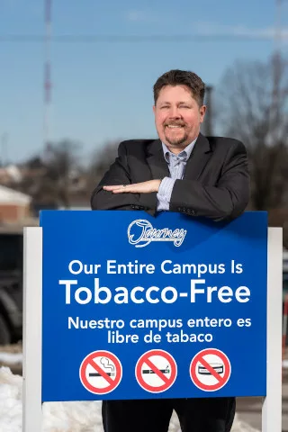 A man posing behind a sign that says 'our entire campus is tobacco-free'
