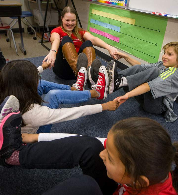Students having fun while sitting by working together to hold hands while touching the bottoms of their feet in the air