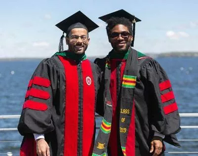 Two students in graduation attire posing lakeside