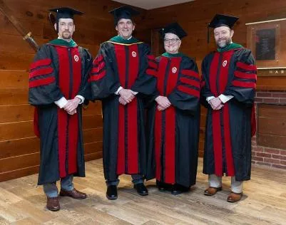 Four faculty members posing together in graduation gowns