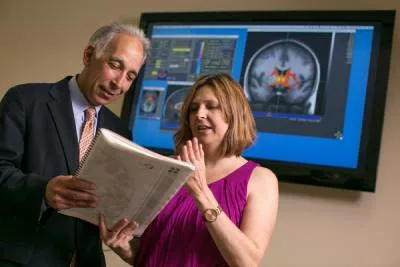 Two researchers analyzing a scientific paper next to a TV displaying a brain scan