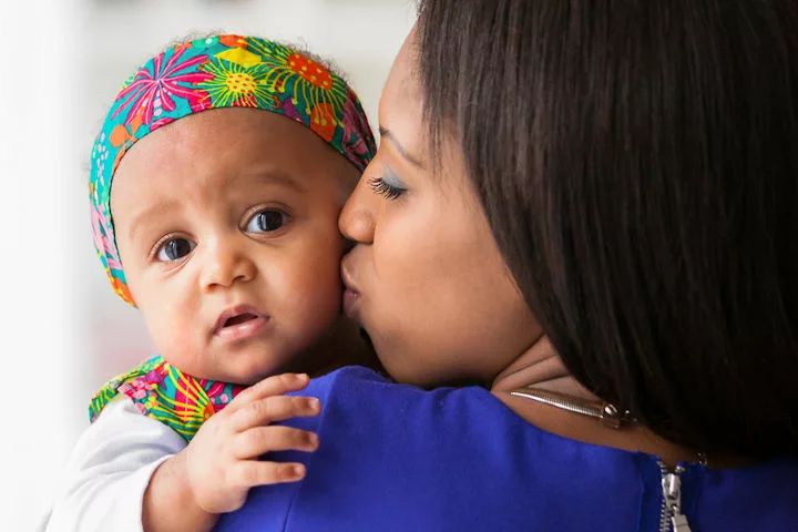 A mother holding a baby and kissing its cheek