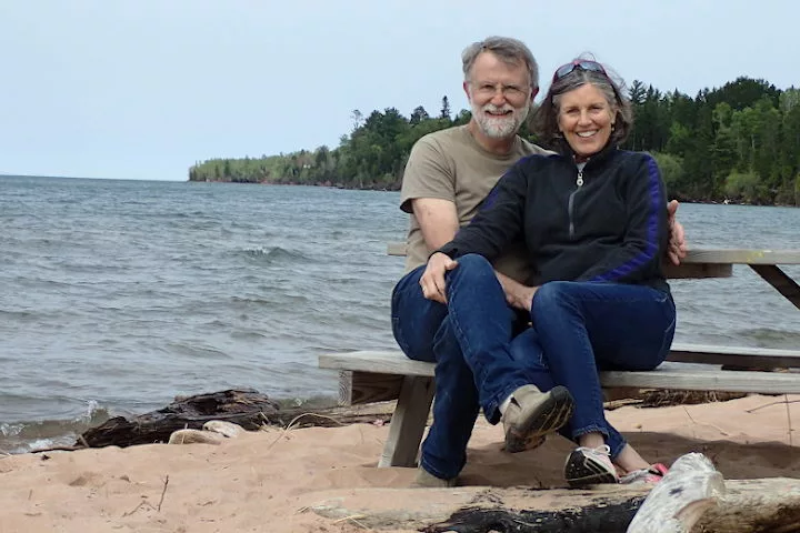 Pat and Kate Remington smiling on a picnic bench by the water